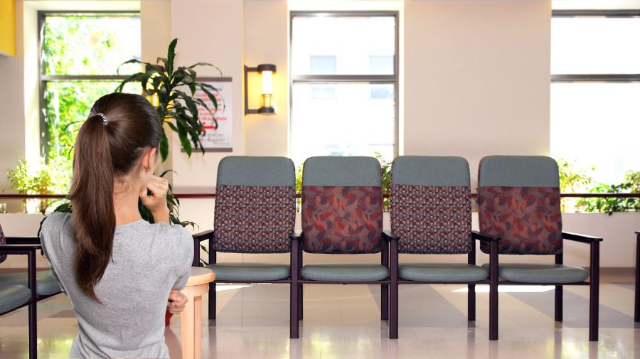an image of a mostly empty waiting room at a care facility, with a woman sitting with her back to us