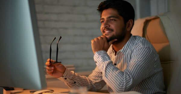 man sitting at a desk, holding glasses and smiling
