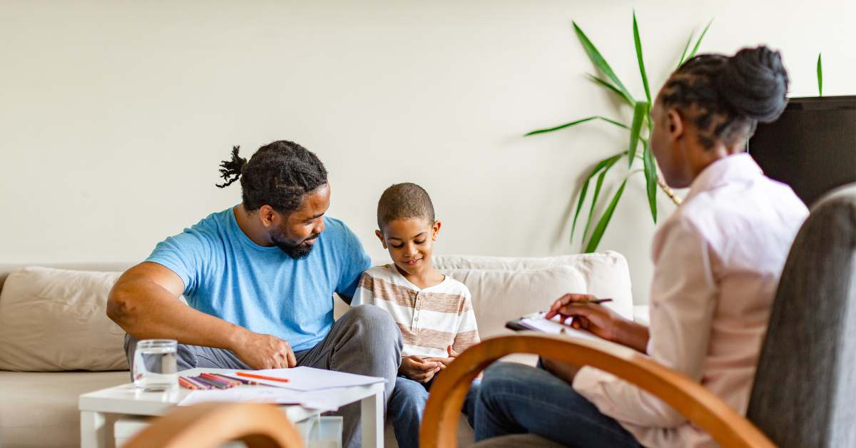 caregiver sitting on couch with young boy across from a therapist