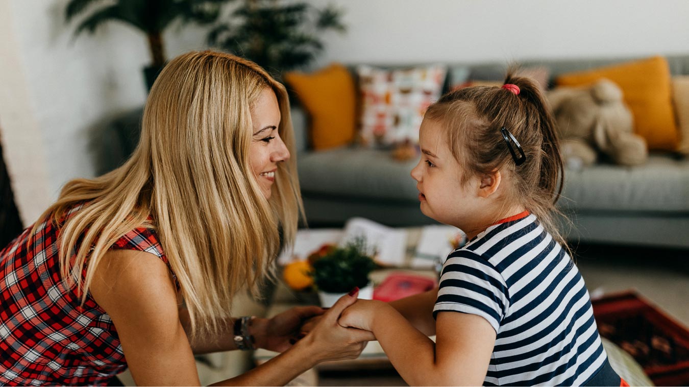 caregiver kneeling in front of a small girl, holding her hand and smiling